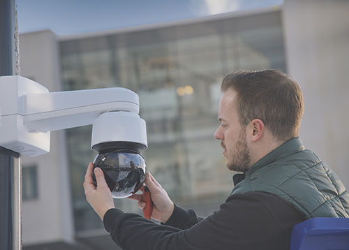 CCTV technician installing an outdoor PTZ video camera on a pole mount.