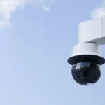 Outdoor AXIS PTZ video camera with laser focus mounted to a wall.