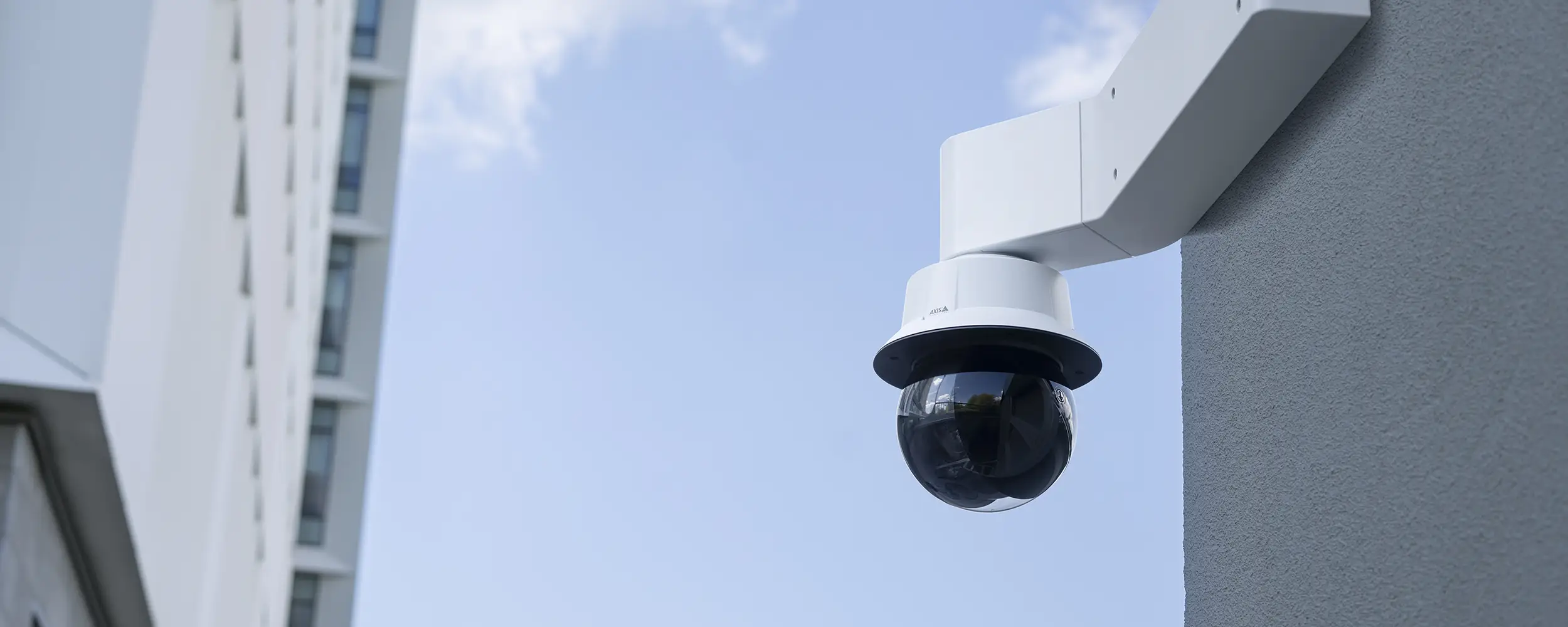 Outdoor AXIS PTZ video camera with laser focus mounted to a wall.