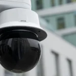 An AXIS Q6325-LE PTZ Video Camera with smoked dome mounted outside a building.