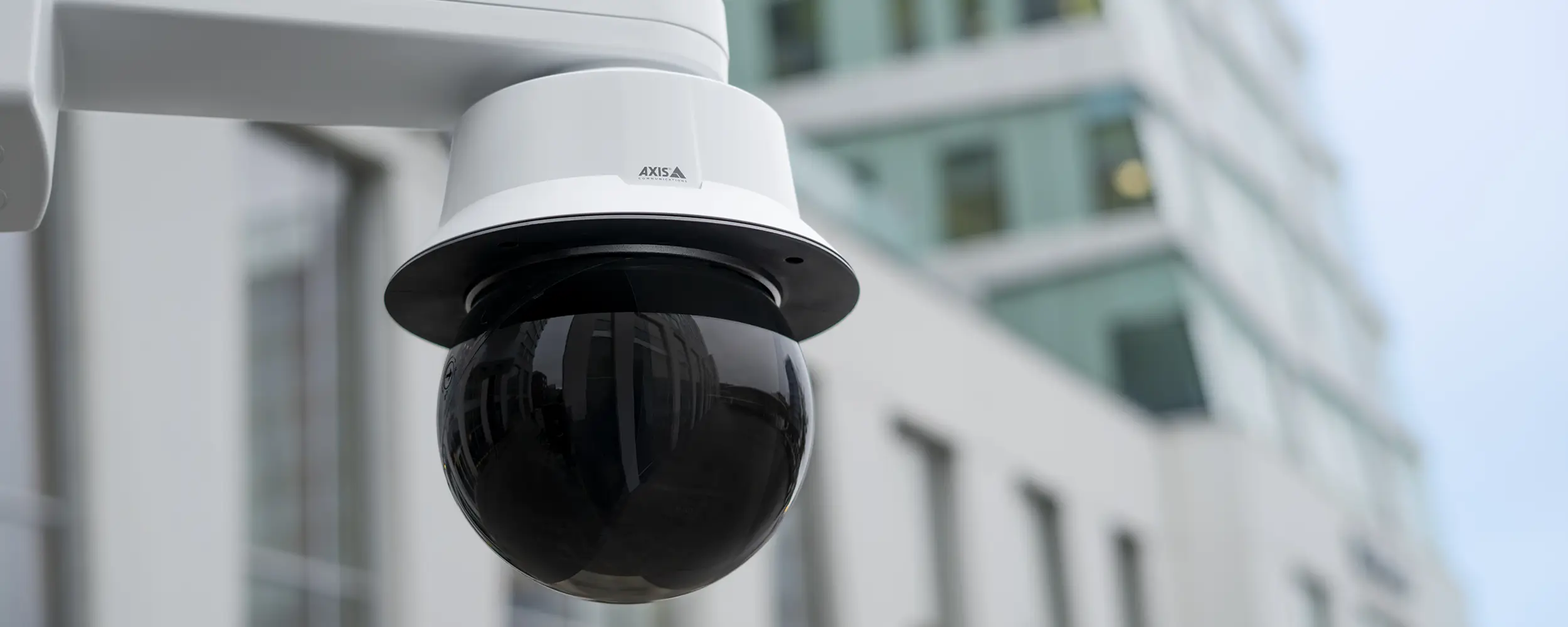 An AXIS Q6325-LE PTZ Video Camera with smoked dome mounted outside a building.